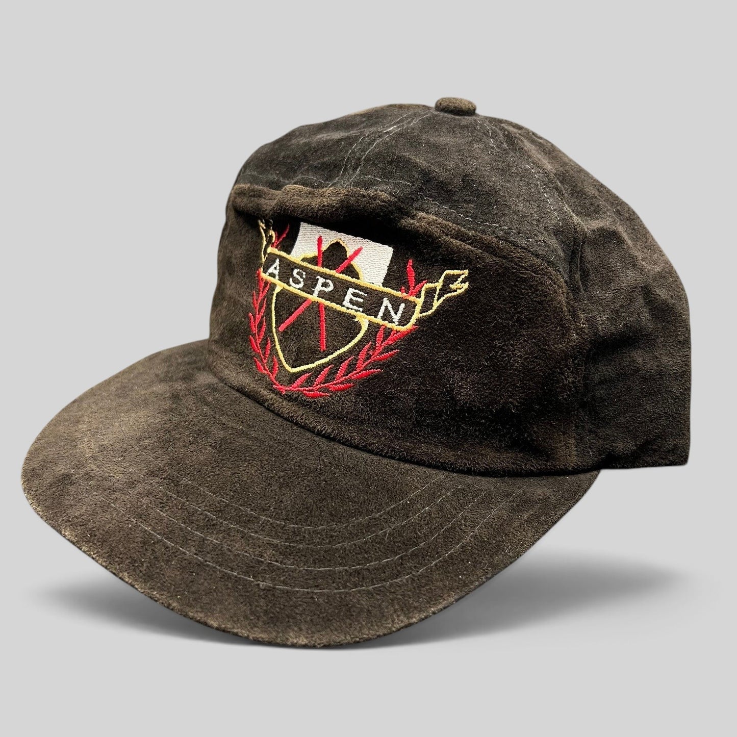 Raree Finds vintage black suede Aspen strapback hat with embroidered crest logo and gold, red, and white accents.