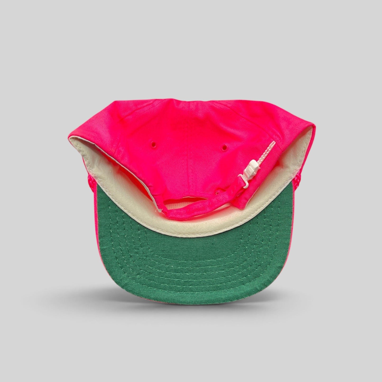 Raree Finds vintage 1980s neon pink snapback hat with a green undervisor and white plastic zipperback closure.