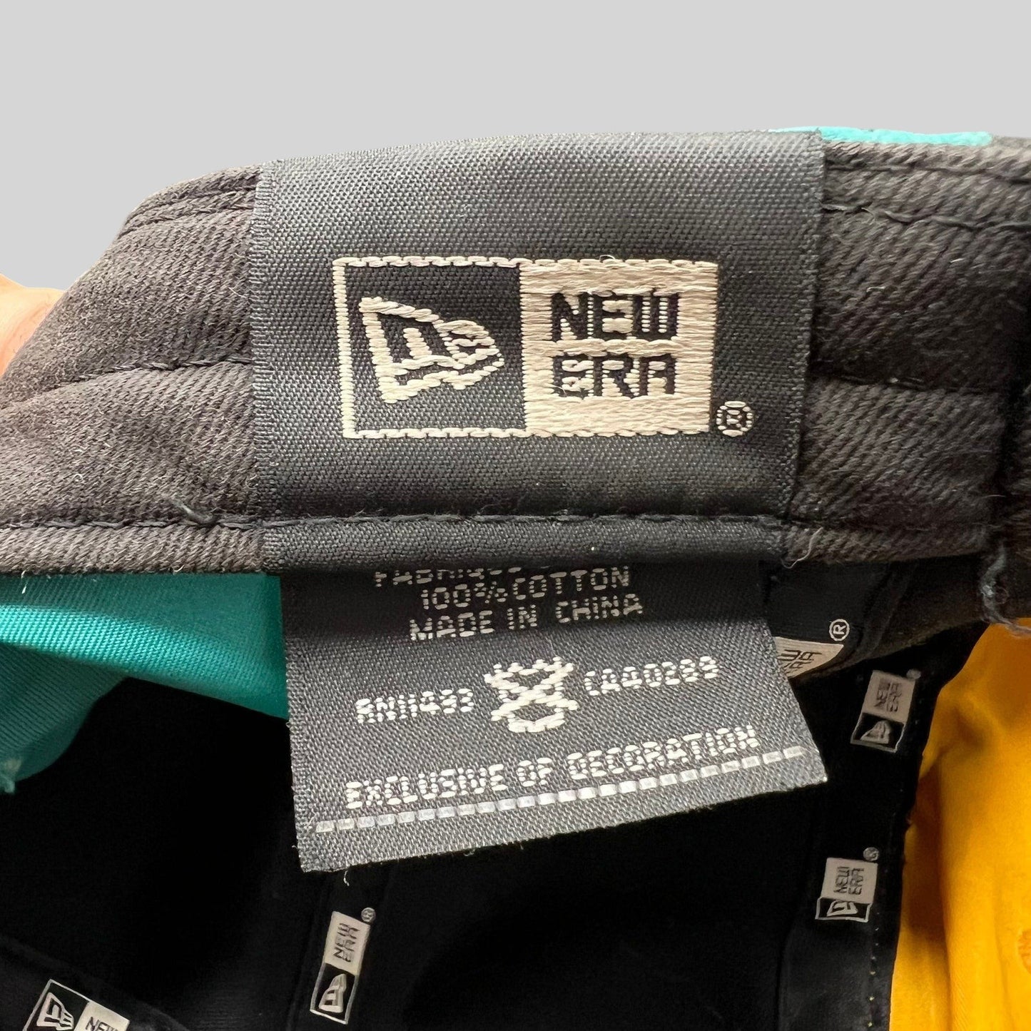 Raree Finds New Era cotton hat interior tag showing brand logo and material details with teal and yellow panels