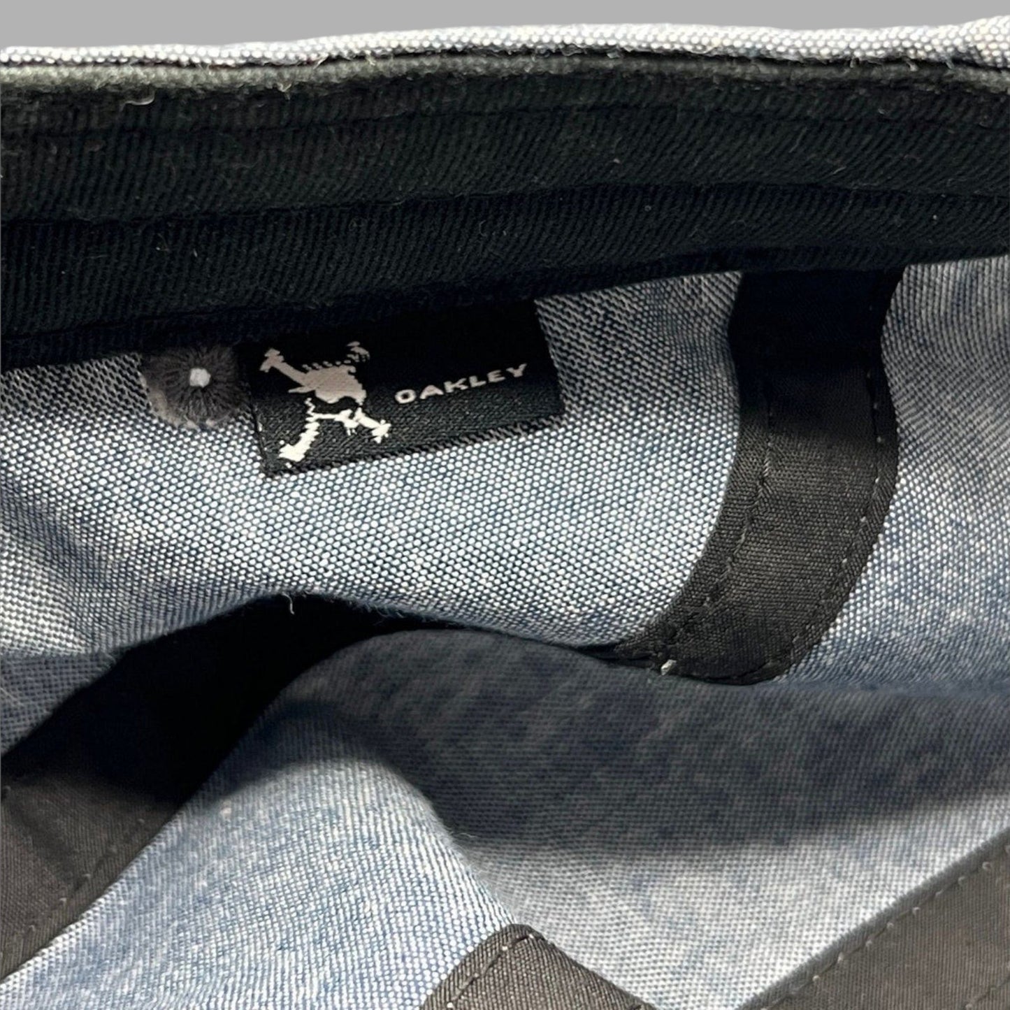 Raree Finds Oakley 5-panel cap interior showing the black skull logo brand tag on light denim chambray fabric