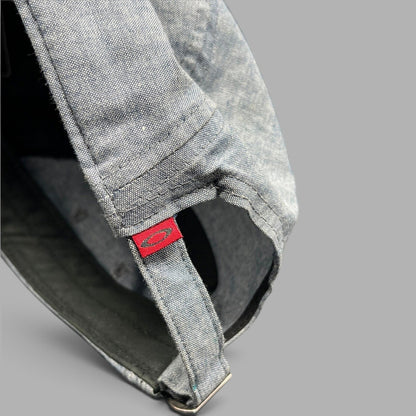 Raree Finds Oakley light denim chambray 5-panel cap showing the red skull logo tag and metal buckle strap detail