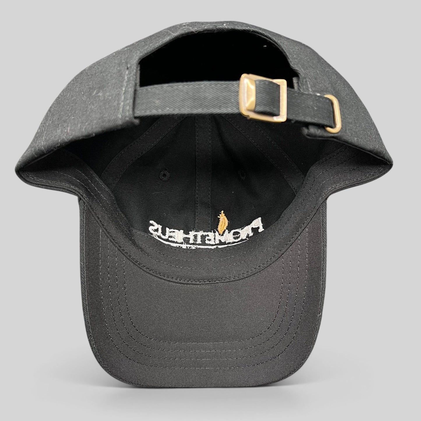 Raree Finds black Yupoong strapback hat with adjustable brass buckle, showing interior embroidery of Prometheus logo.