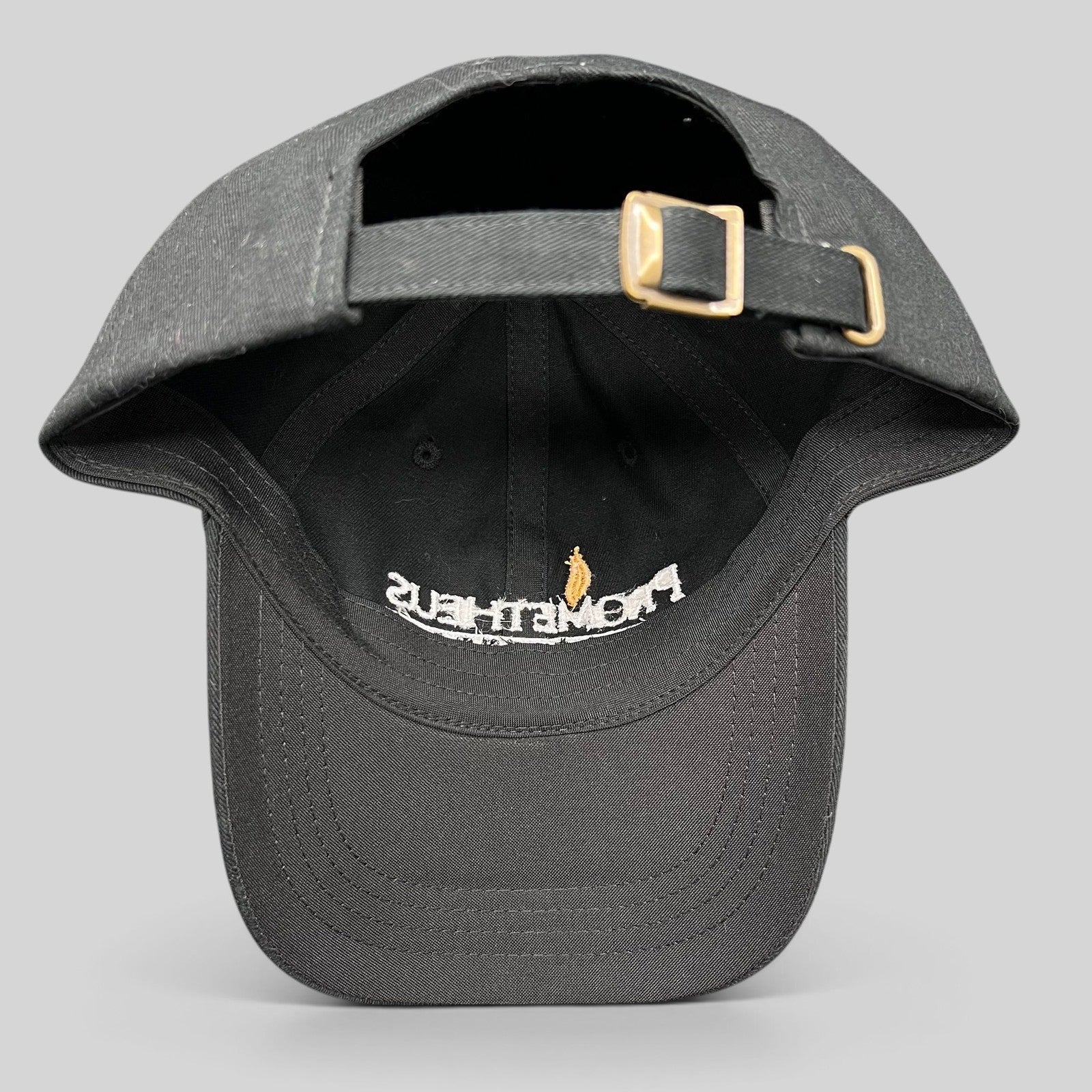 Raree Finds black Yupoong strapback hat with adjustable brass buckle, showing interior embroidery of Prometheus logo.