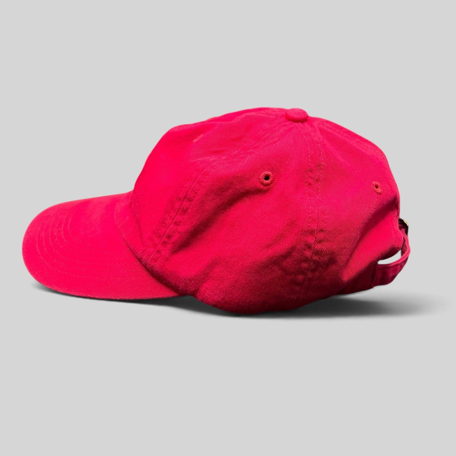 Raree Finds red cotton unstructured strapback hat with embroidered logo, side profile view.