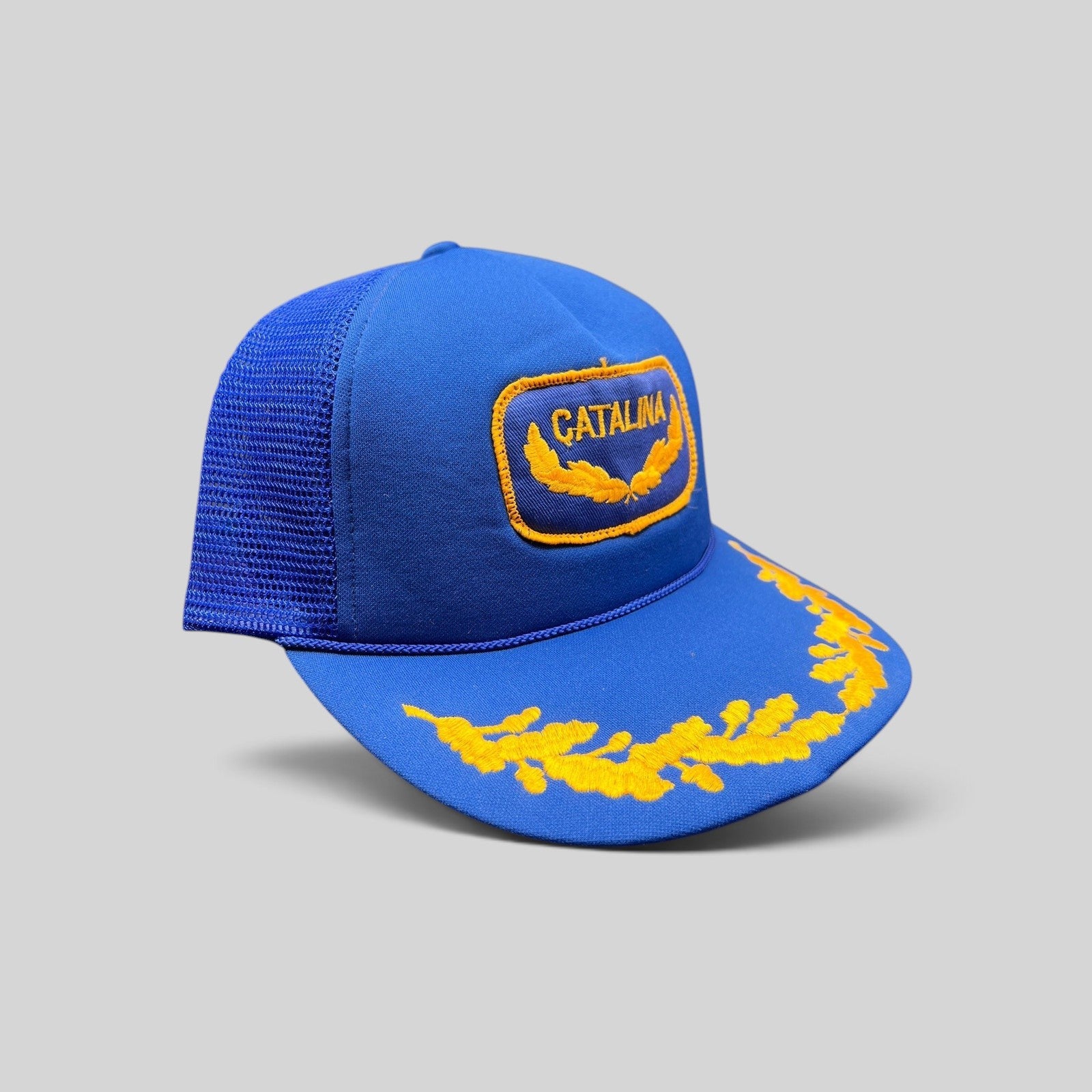 Raree Finds vintage 1980s royal blue foam trucker hat with gold Catalina patch and laurel leaf embroidery on the brim.