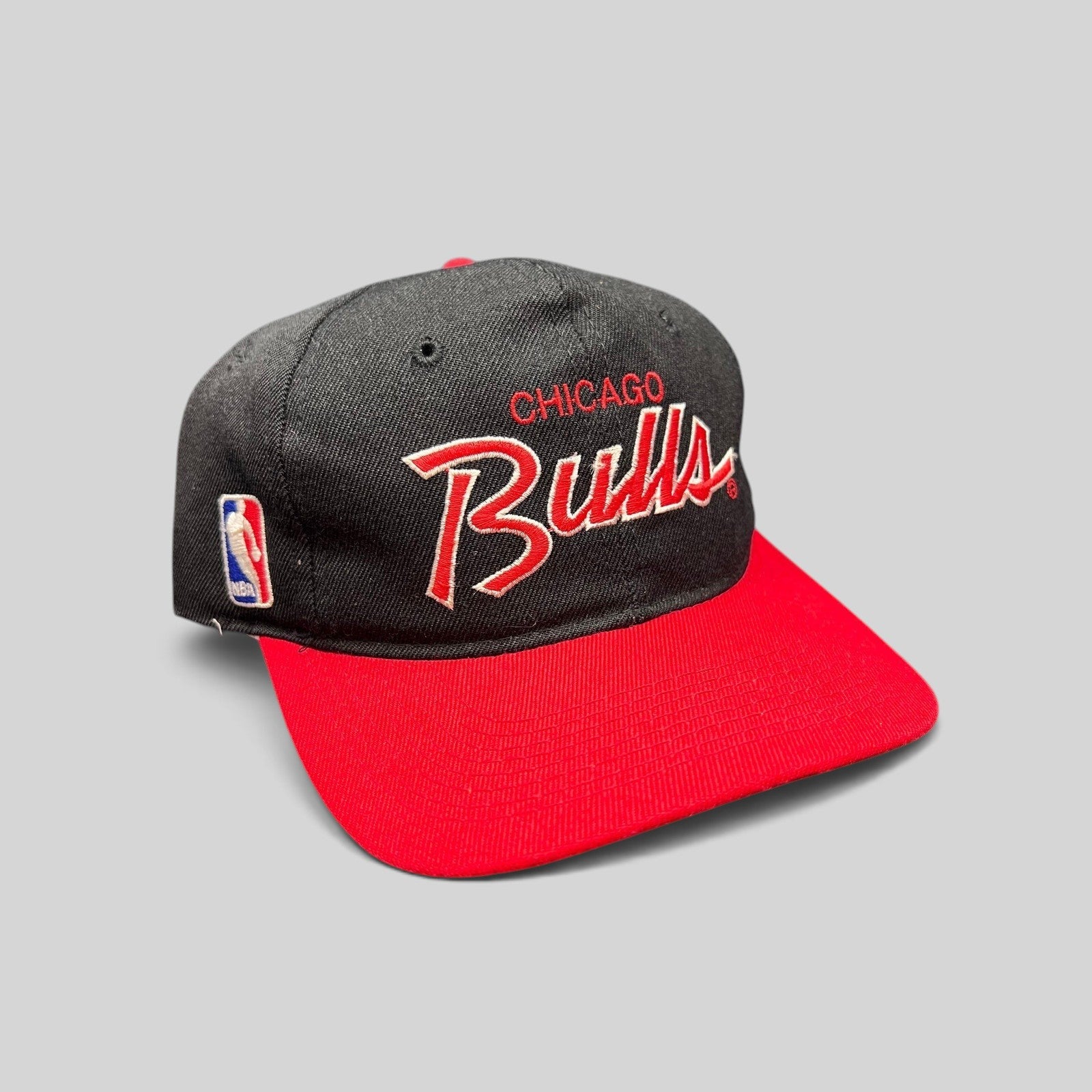 Raree Finds vintage 90s Chicago Bulls script snapback hat with black crown, red brim, and embroidered NBA logo.