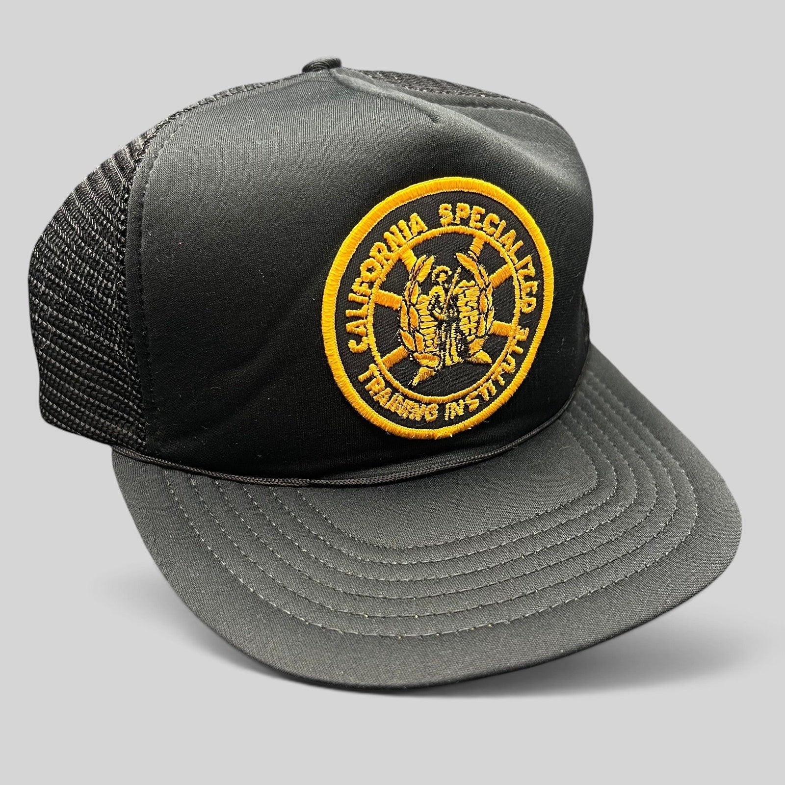 Raree Finds vintage black foam trucker hat with a gold California Specialized Training Institute embroidered patch.