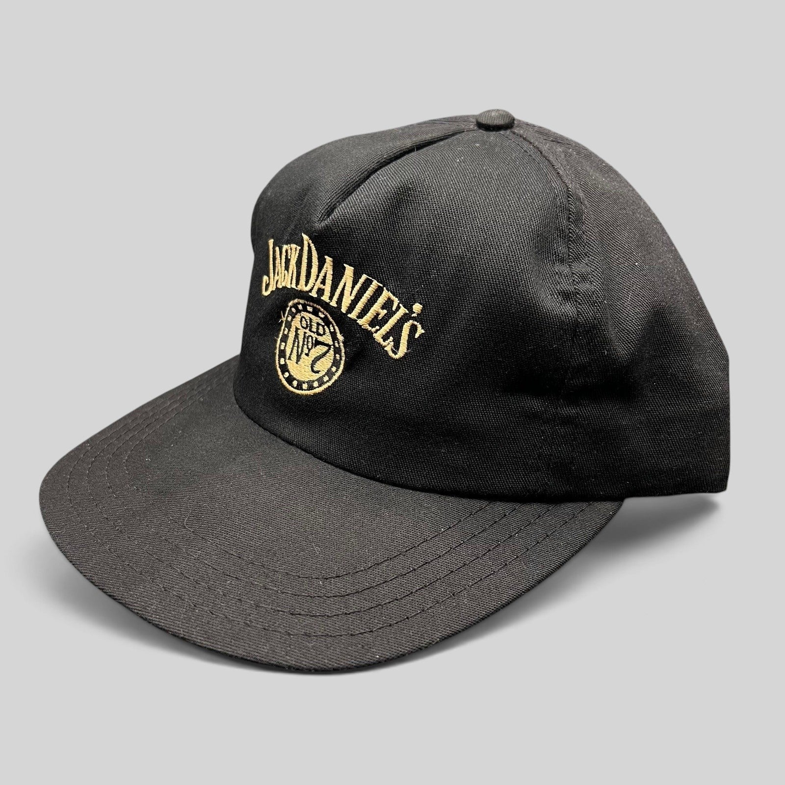Raree Finds vintage 90s black Jack Daniel’s snapback hat with gold embroidered Old No. 7 logo and curved visor.