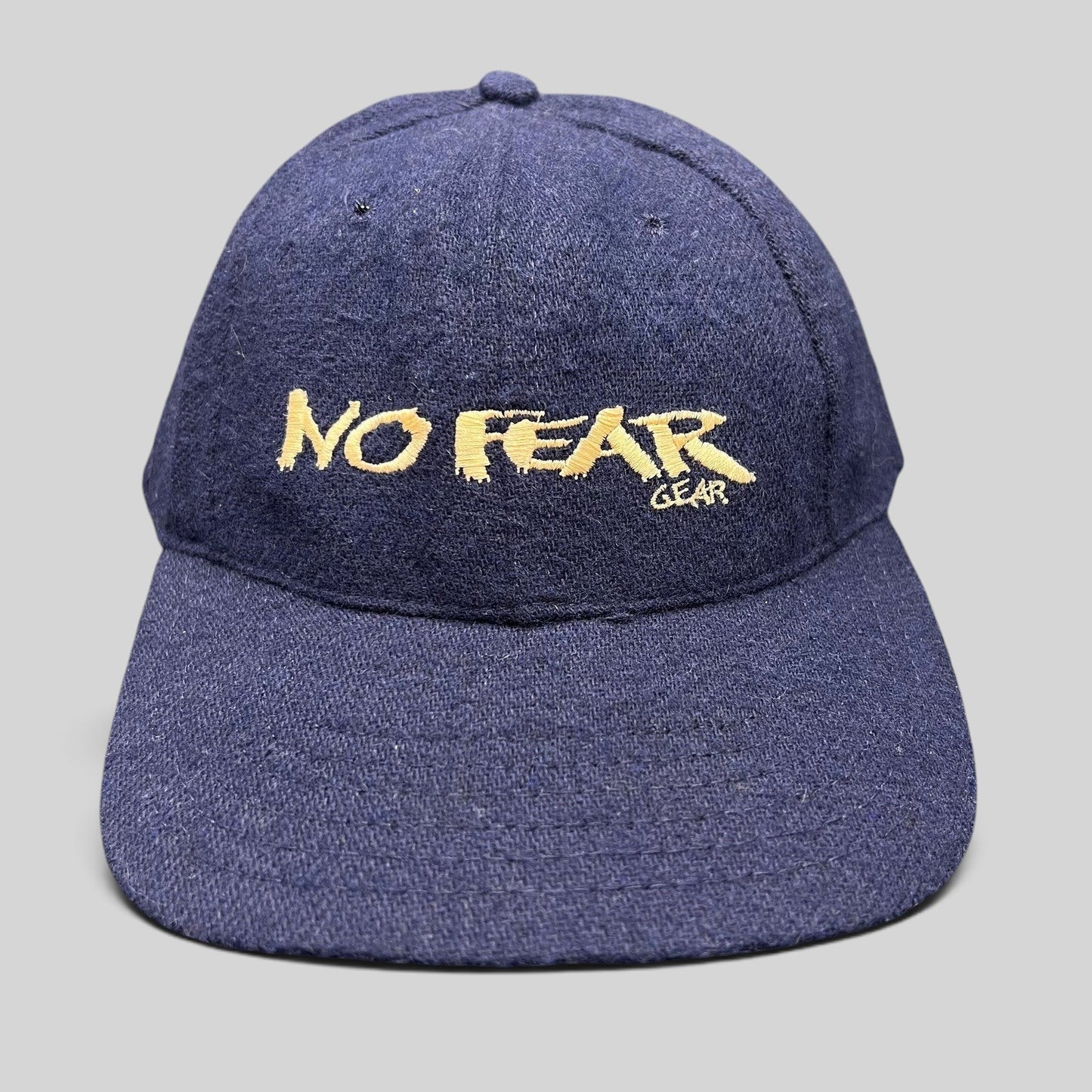 Raree Finds vintage 90s navy wool-blend snapback hat with gold No Fear Gear embroidery and structured six-panel design.