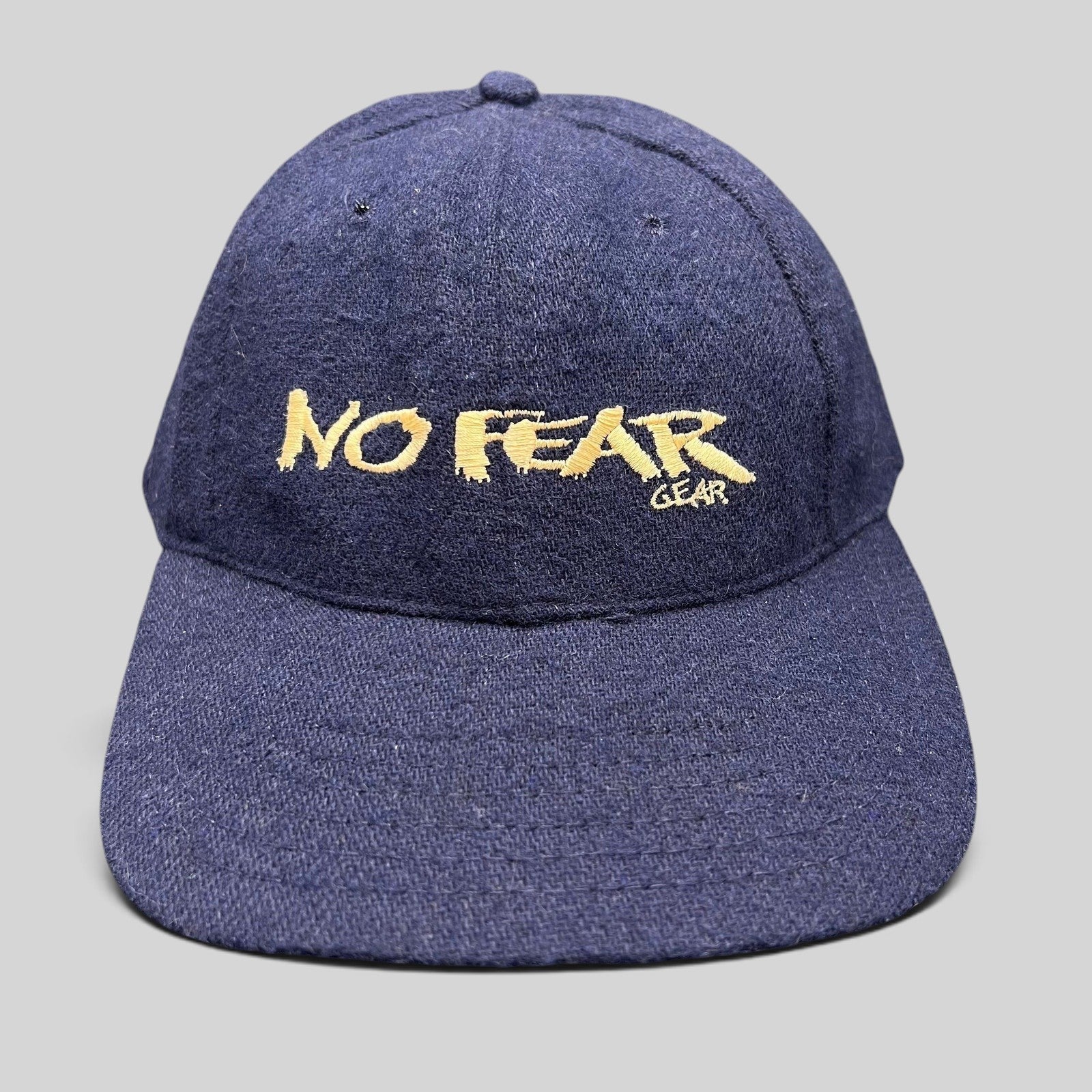 Raree Finds vintage 90s navy wool-blend snapback hat with gold No Fear Gear embroidery and structured six-panel design.