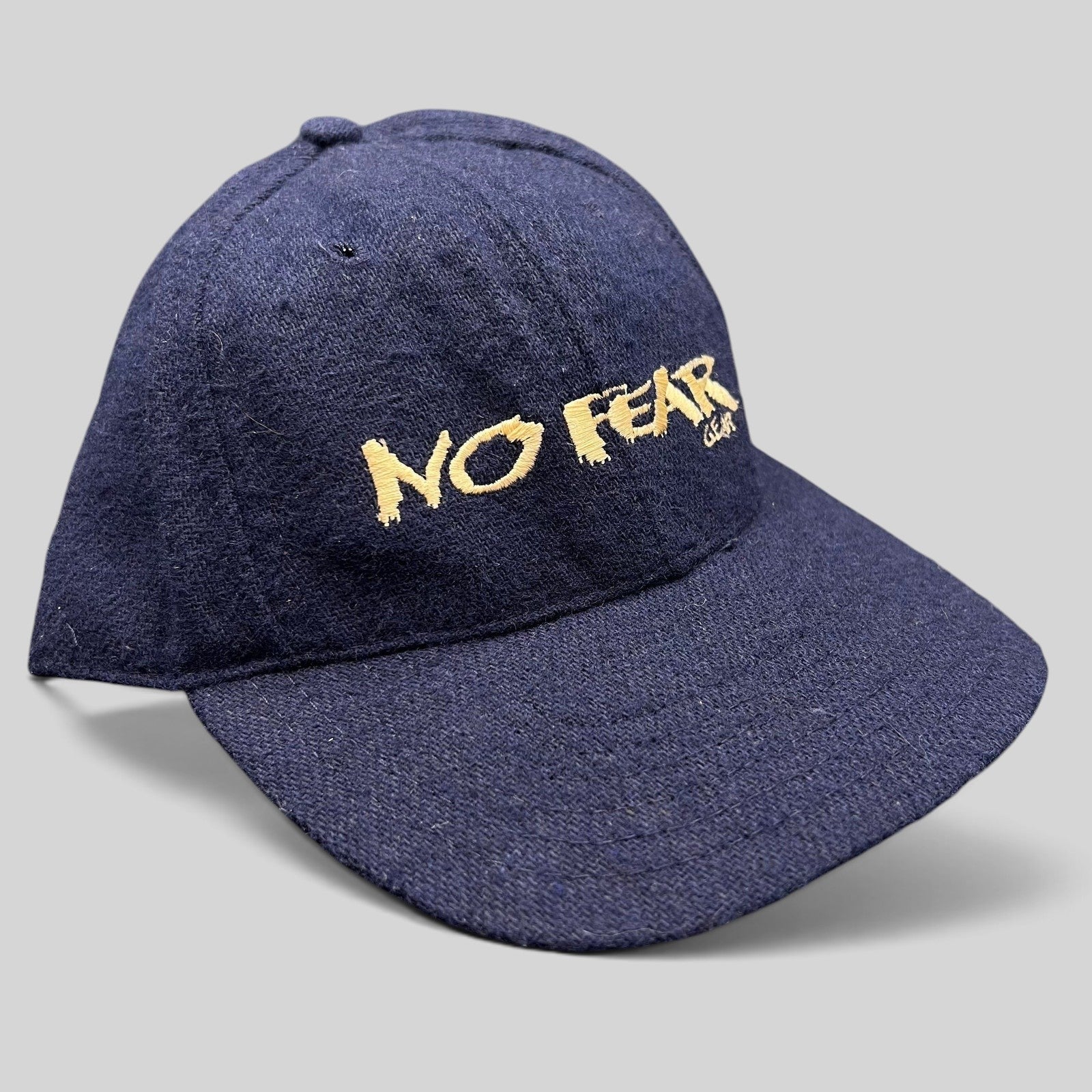 Raree Finds vintage 90s navy wool-blend snapback hat with gold No Fear Gear embroidery and structured six-panel design.
