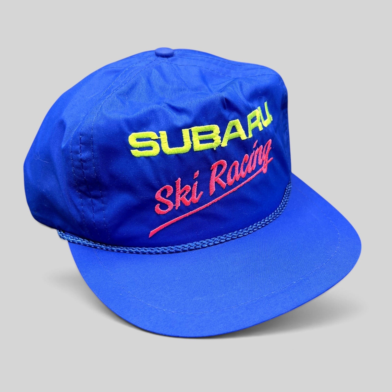 Raree Finds vintage blue nylon Subaru Ski Racing strapback hat with neon embroidery and rope detail on the brim.