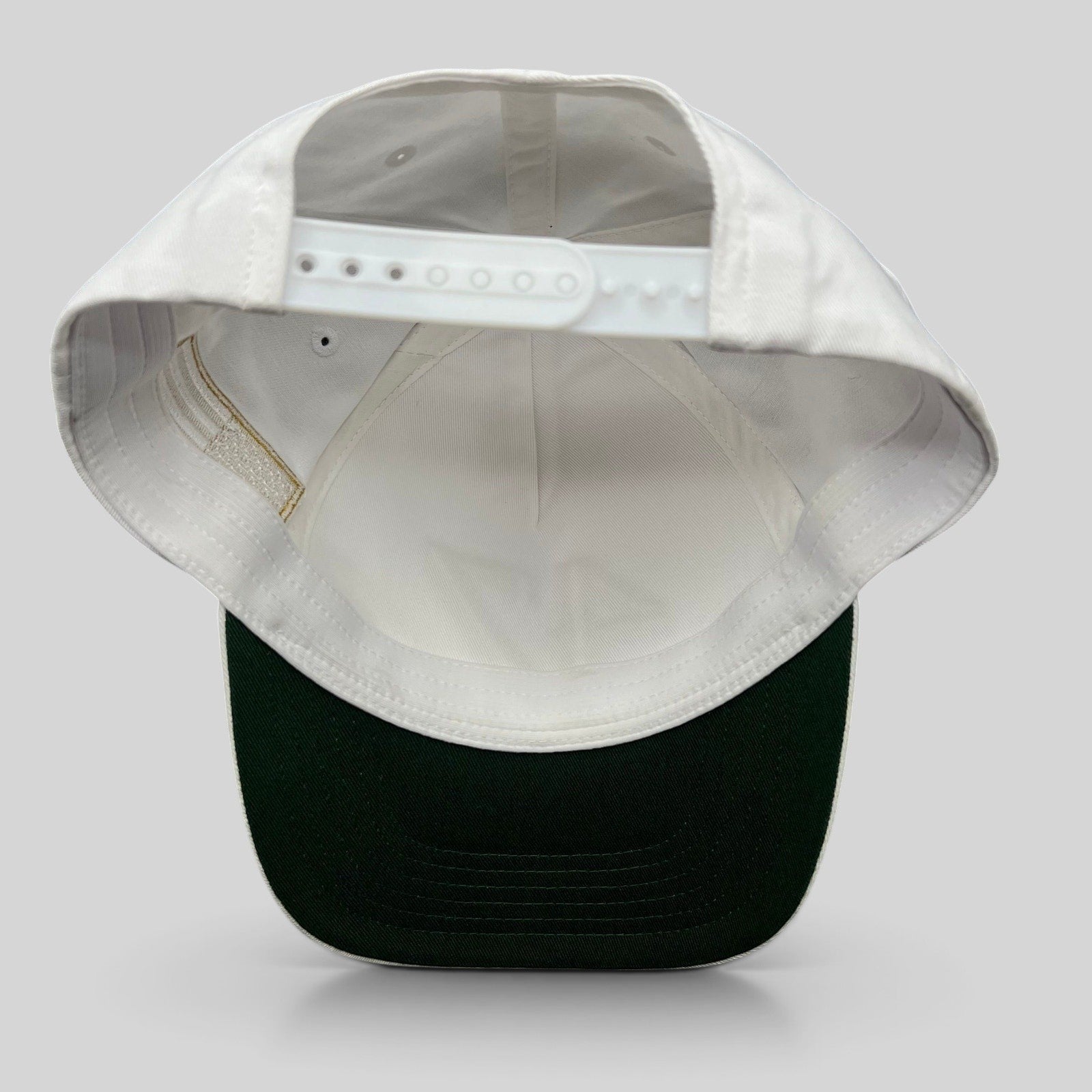 Raree Finds white cotton snapback hat with a green undervisor and adjustable plastic snap closure, back view.